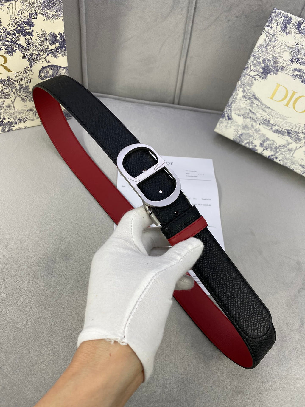 Dior belt close-up on hand: black strap with red edge and silver buckle.