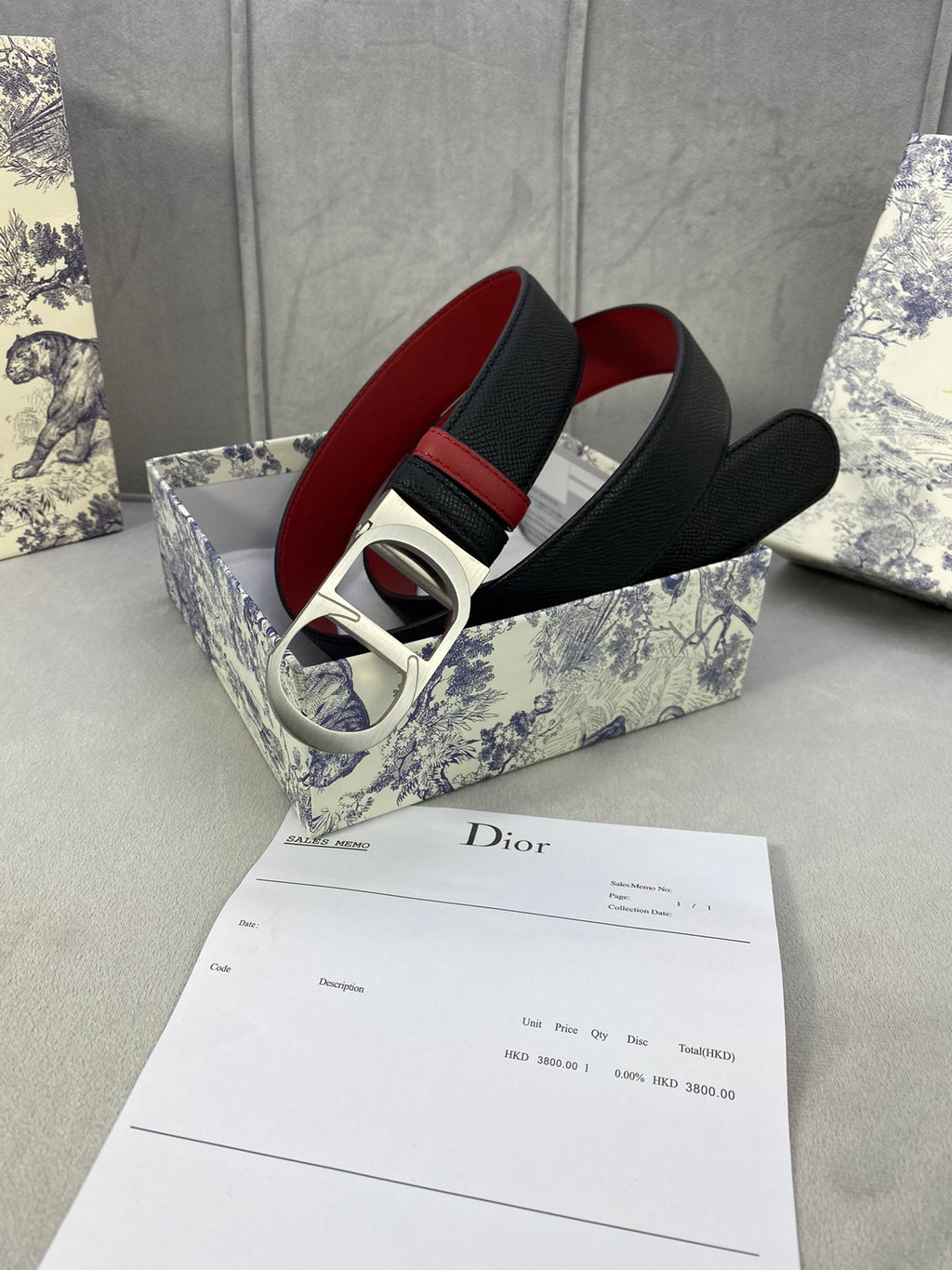 Dior belt with black textured strap, red-lined edge, silver-tone buckle.