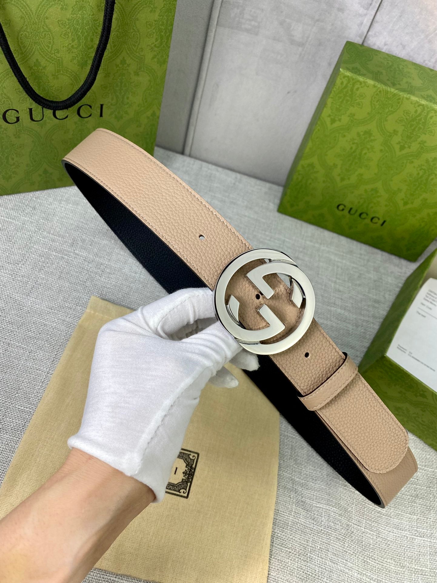 Gucci belt beige leather with silver G buckle, held in hand over dust bag