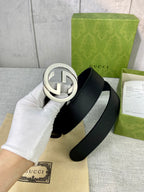 Black leather belt with silver-tone interlocking GG round buckle, close-up.