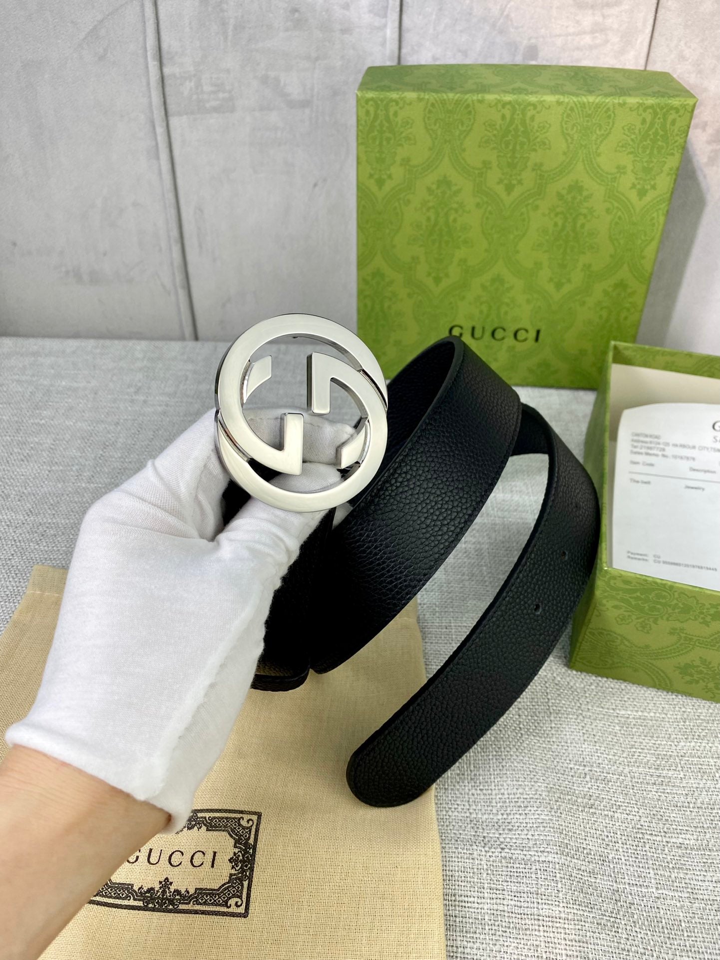 Black leather belt with silver-tone interlocking GG round buckle, close-up.