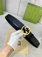 Black leather belt held in hand with gold-tone interlocking GG buckle.