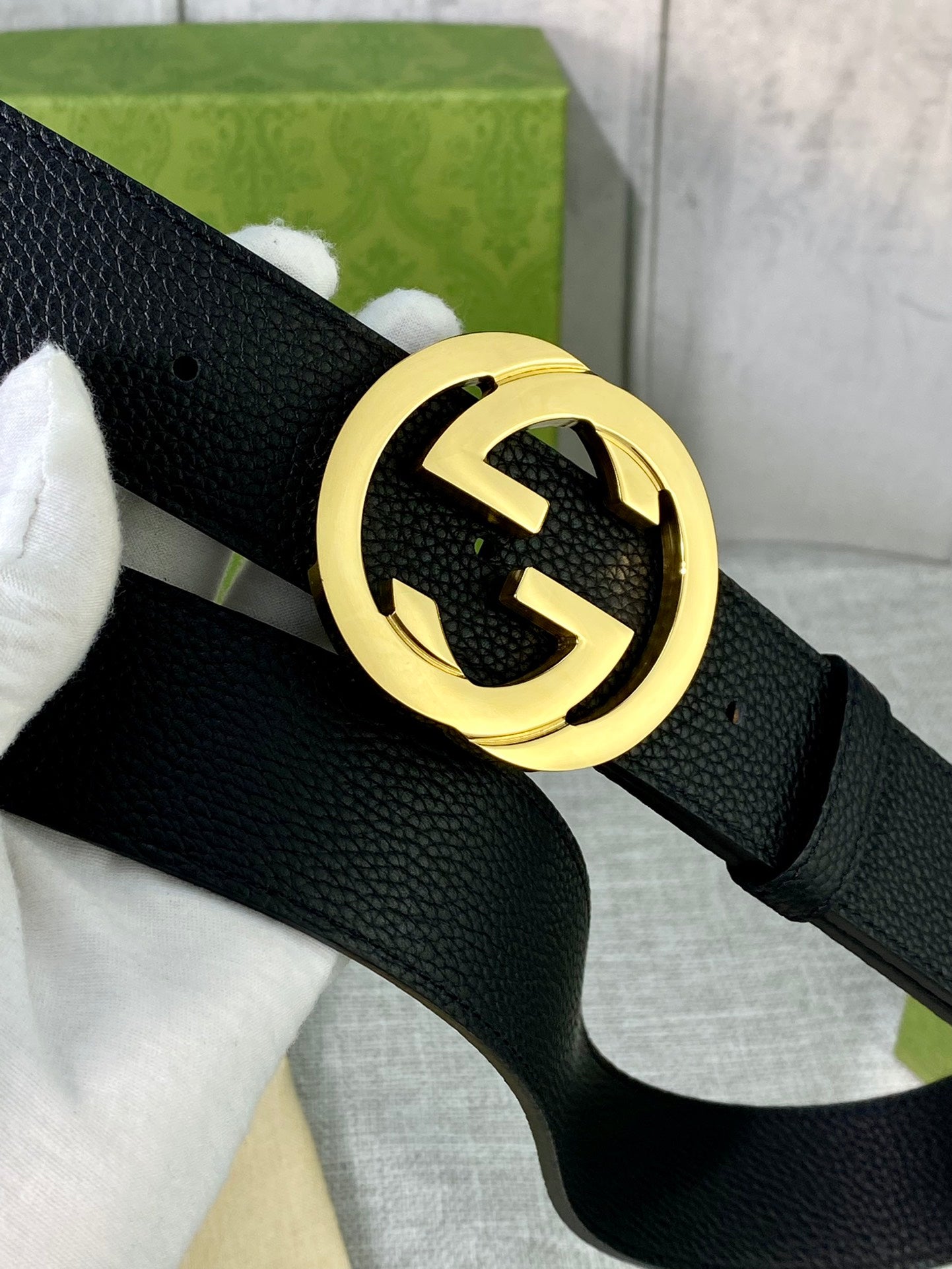 Black leather belt with gold-tone interlocking GG circular buckle, close-up.