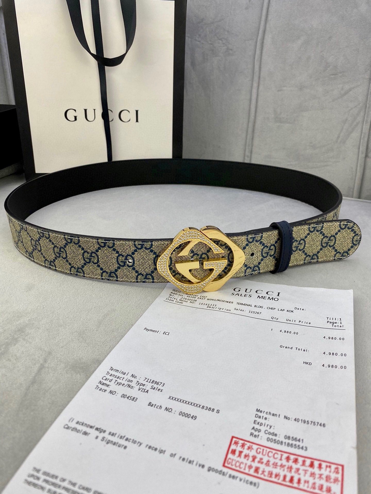 Belt with blue GG monogram strap and gold-tone buckle laid over documents