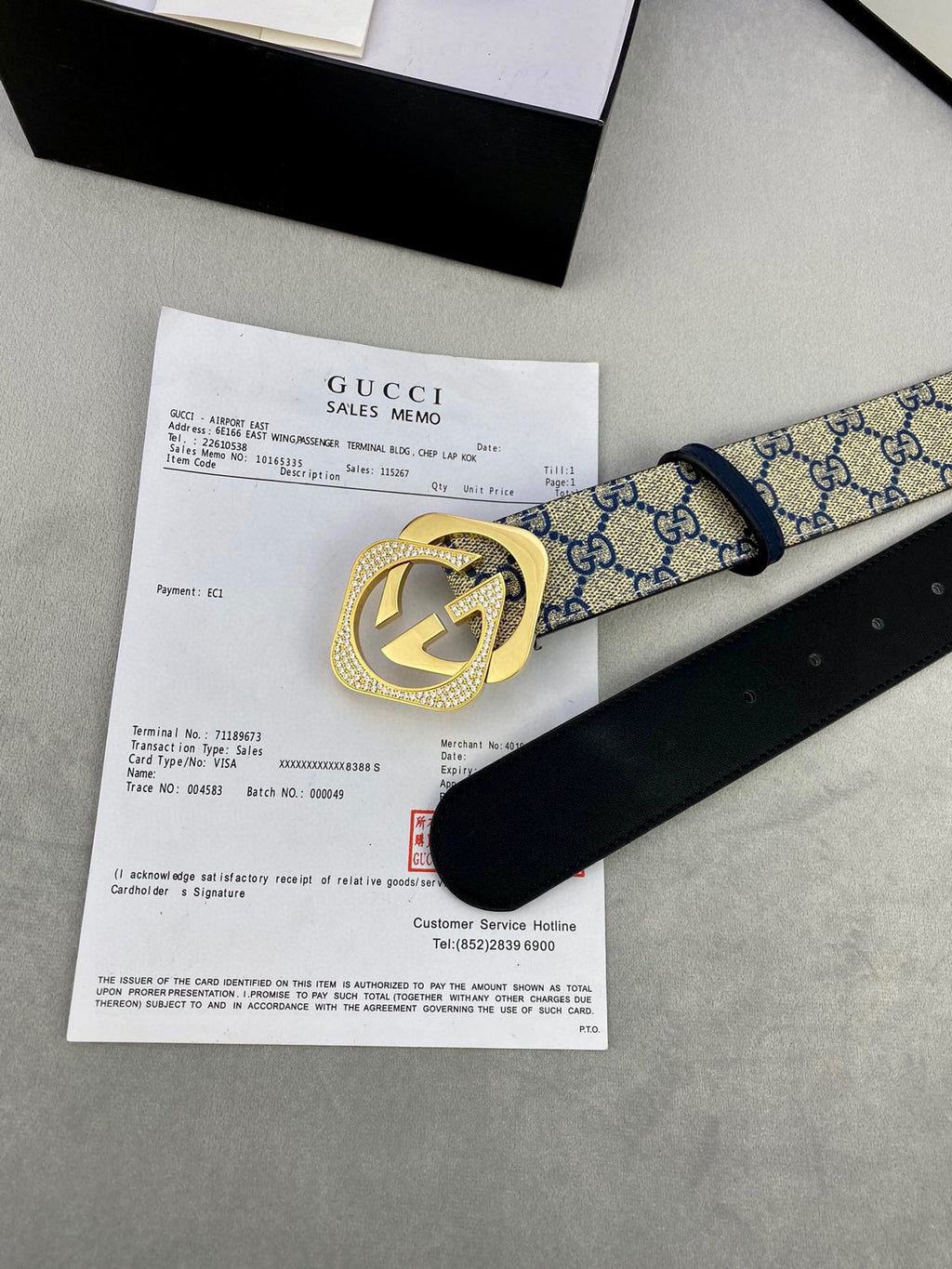 GG monogram belt with gold-tone buckle next to sales memo and black leather strap