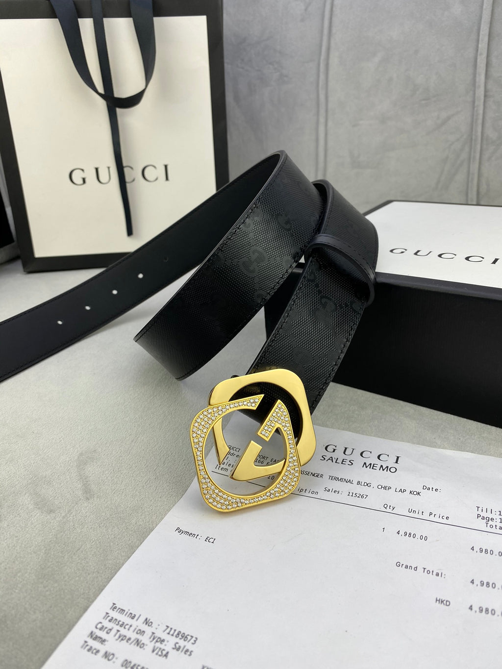 Gucci belt with dark leather strap and gold interlocking buckle, laid across papers.