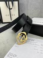 Gucci belt with dark leather strap and gold interlocking buckle, laid across papers.