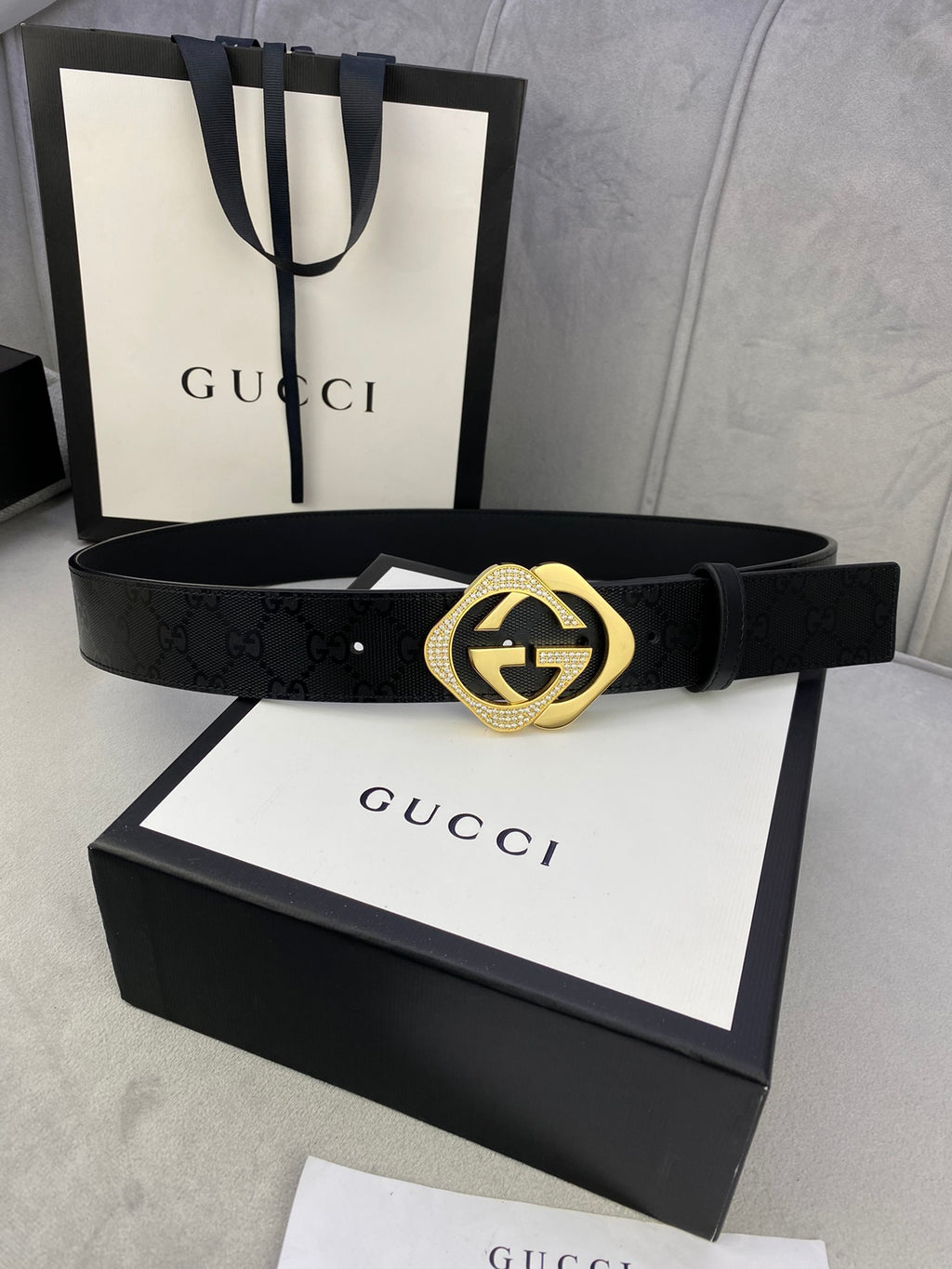 Gucci belt with dark leather strap and gold interlocking buckle, centered on box lid.