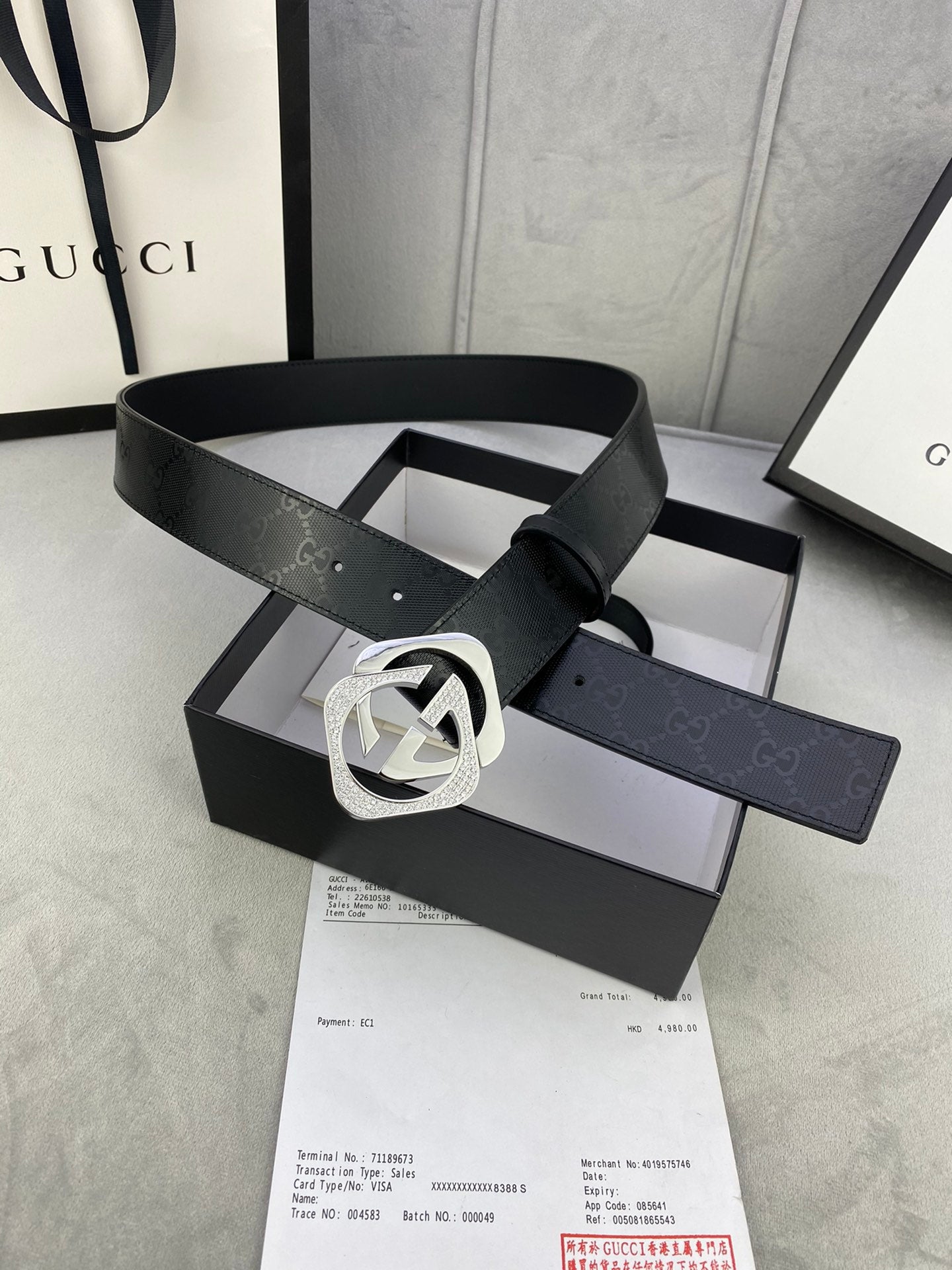 Gucci belt with dark leather strap and silver interlocking buckle, strap tip visible.