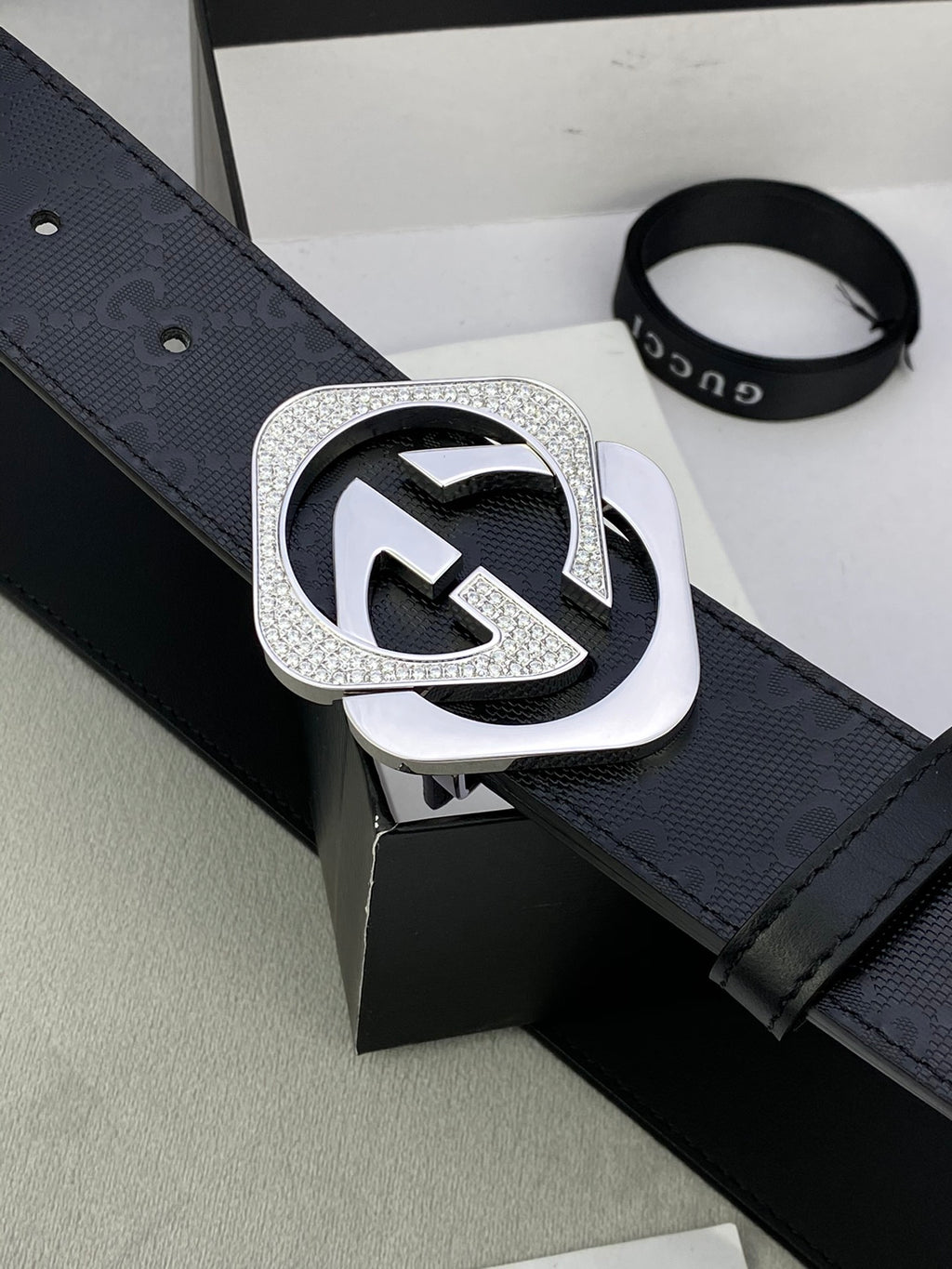 Gucci belt close-up with dark leather strap and large silver interlocking buckle.