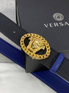 Leather belt close-up: black textured strap with gold Medusa buckle and blue edge