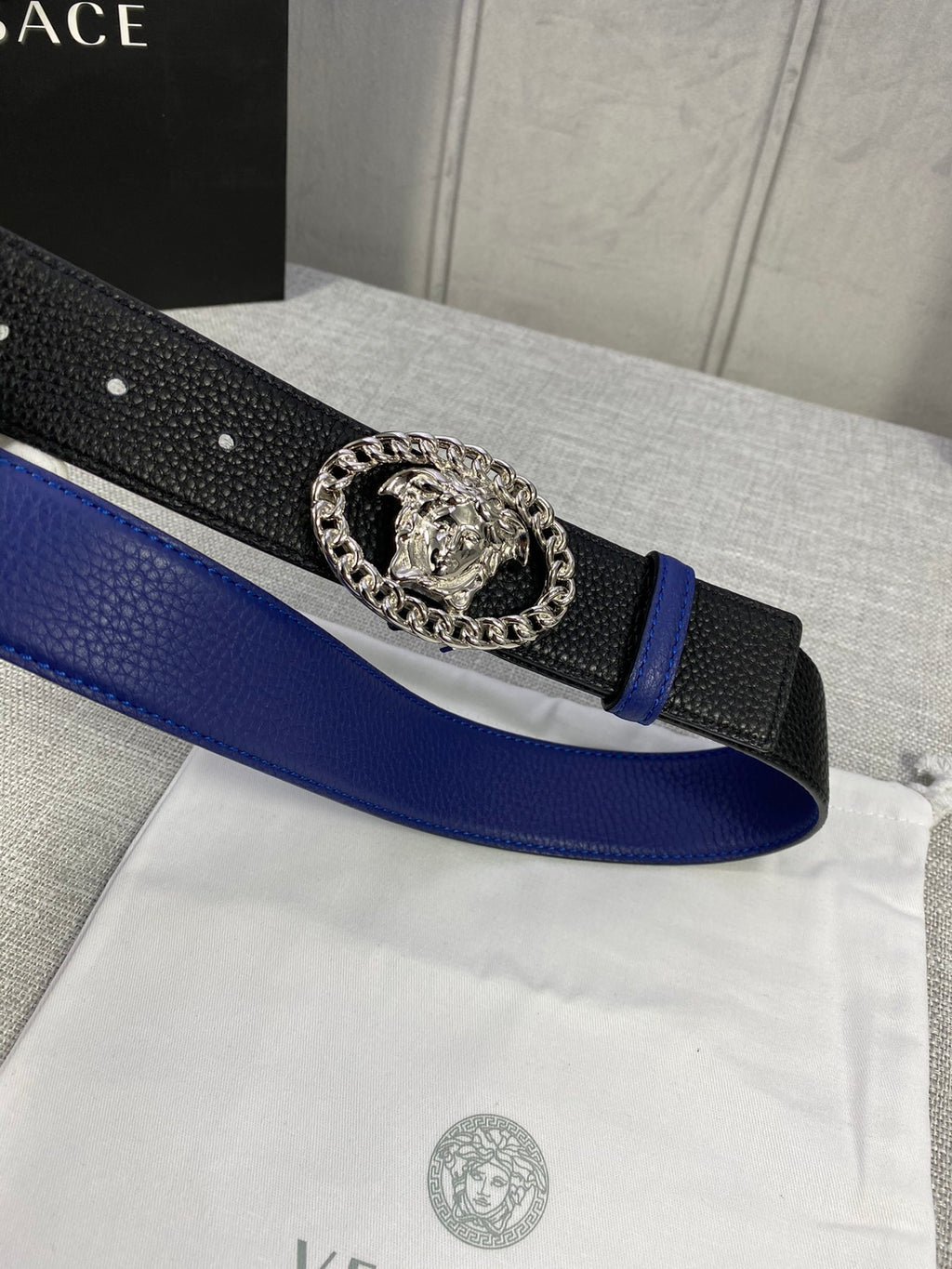 Leather belt close-up with blue strap, black textured band, silver Medusa buckle