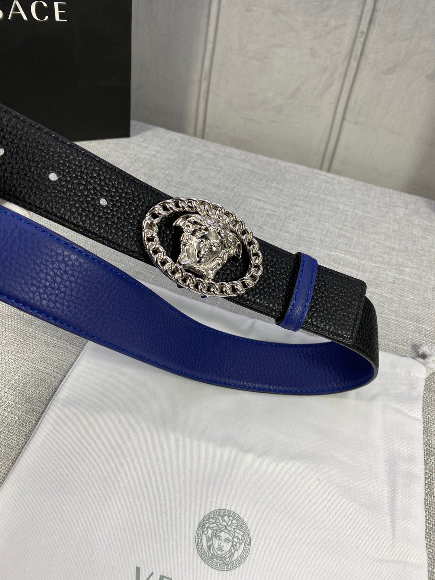 Leather belt close-up with blue strap, black textured band, silver Medusa buckle