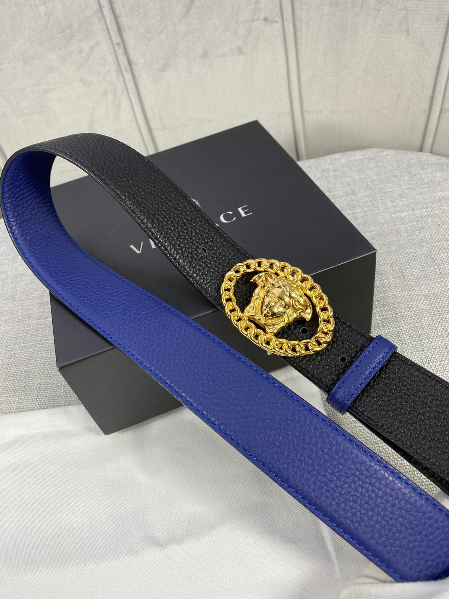 Leather belt laid flat: blue strap with black textured sections and gold Medusa buckle