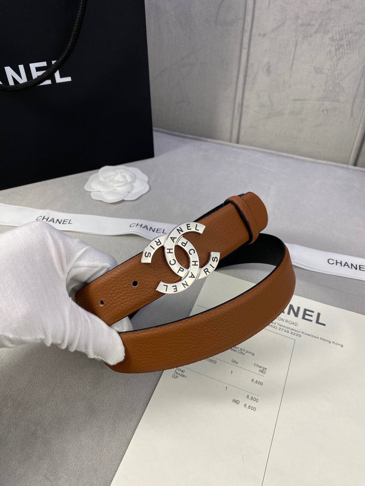 Chanel belt tan-brown leather held in white-gloved hand; gold CHANEL buckle