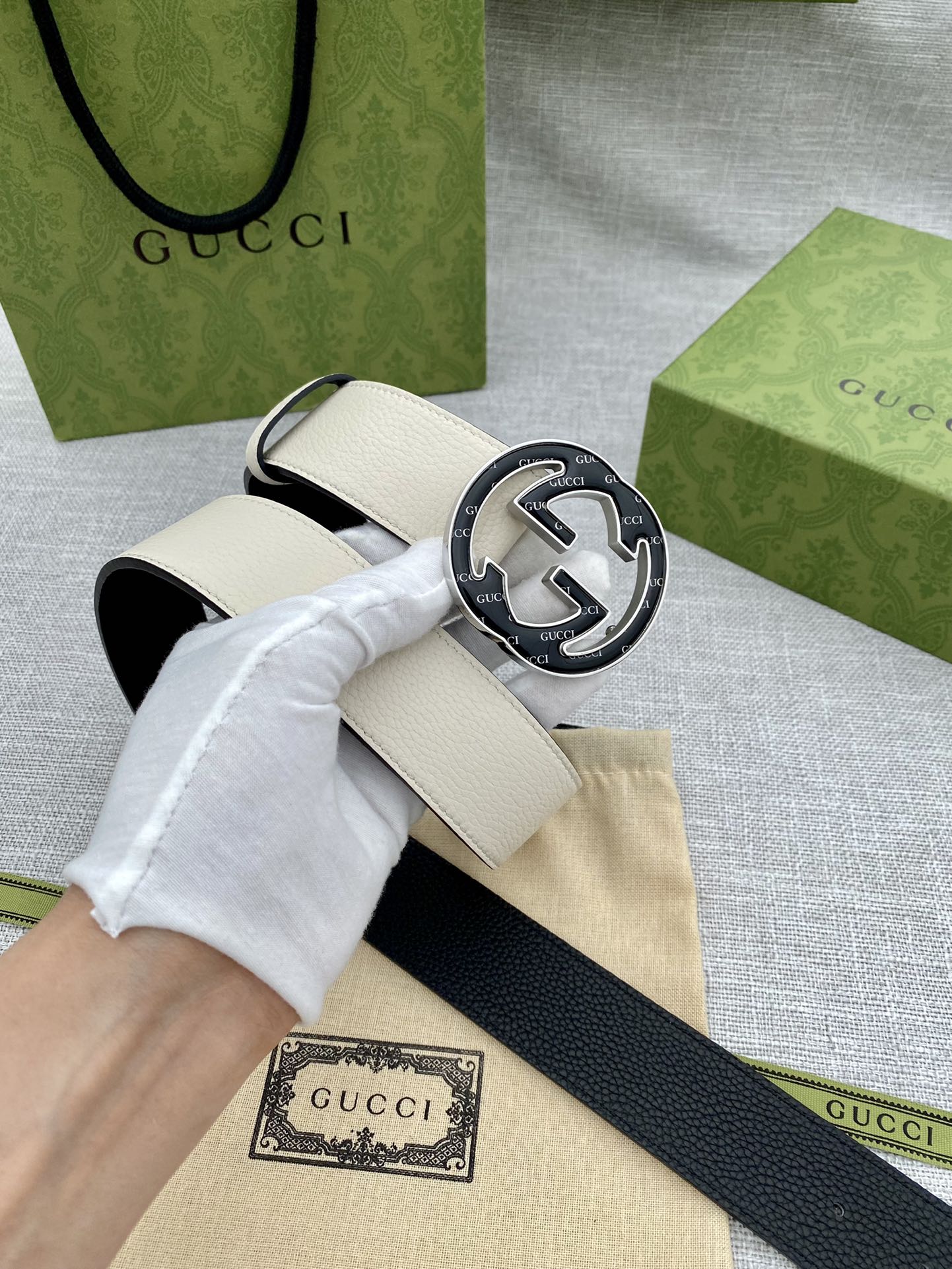 Gucci white leather belt with black GG logo buckle, laid across paper bag