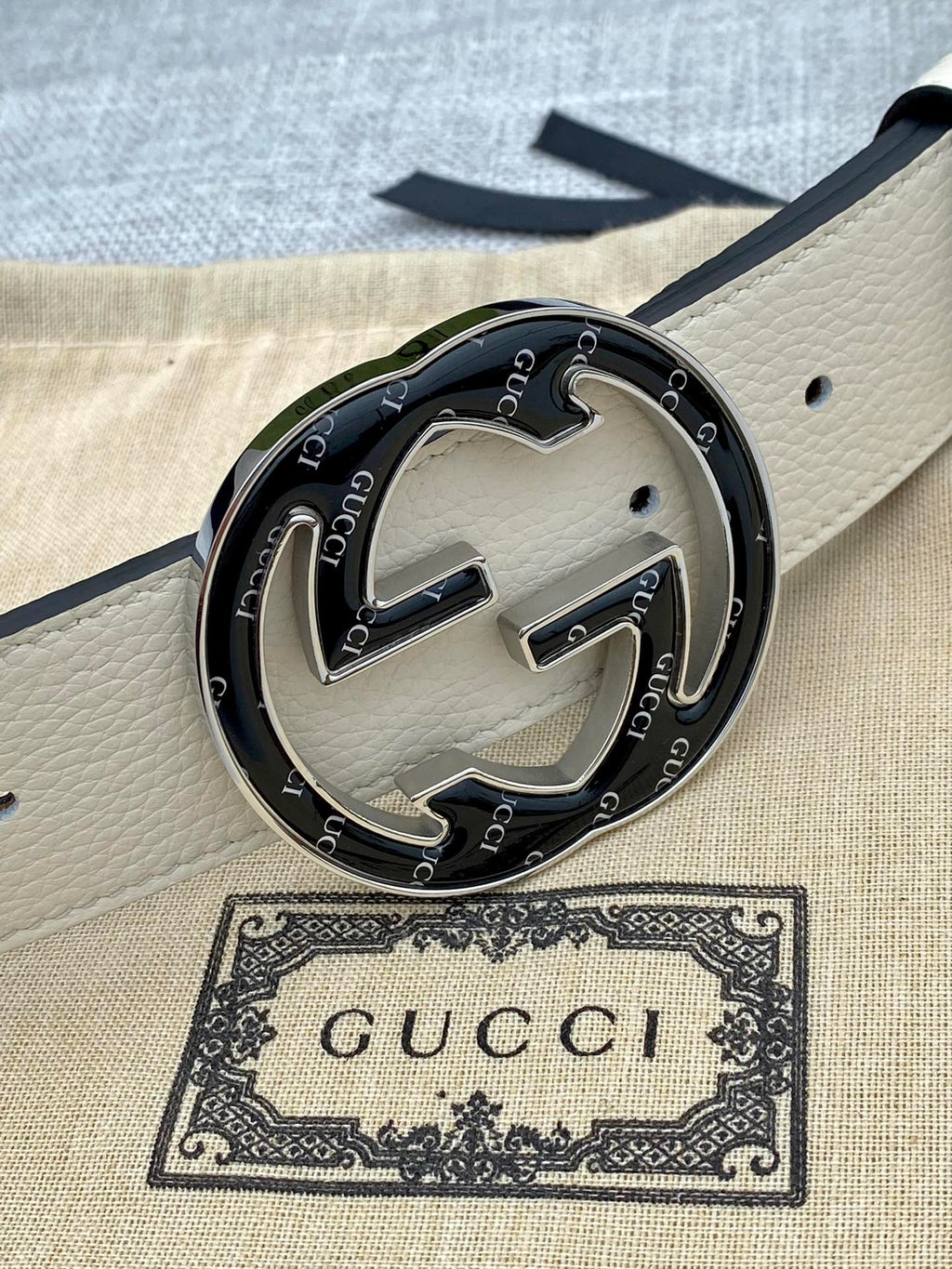 Gucci belt buckle close-up on white strap with black GG interlocking logo