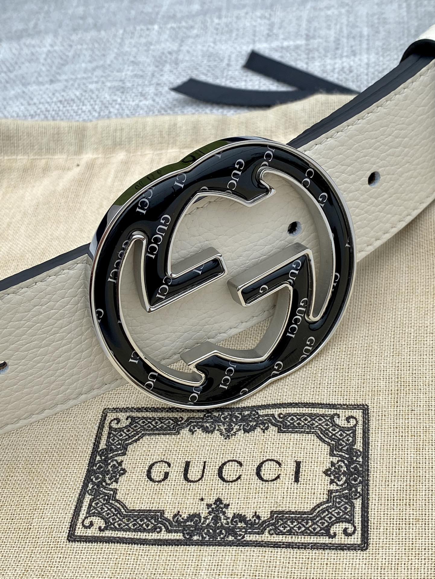 Gucci belt buckle close-up on white strap with black GG interlocking logo