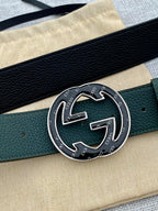 Close-up of dark green leather belt with round GG logo buckle in gold-tone metal