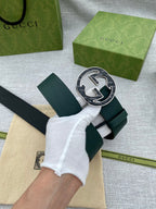 Dark green leather belt with round GG logo buckle, strap held by gloved hand