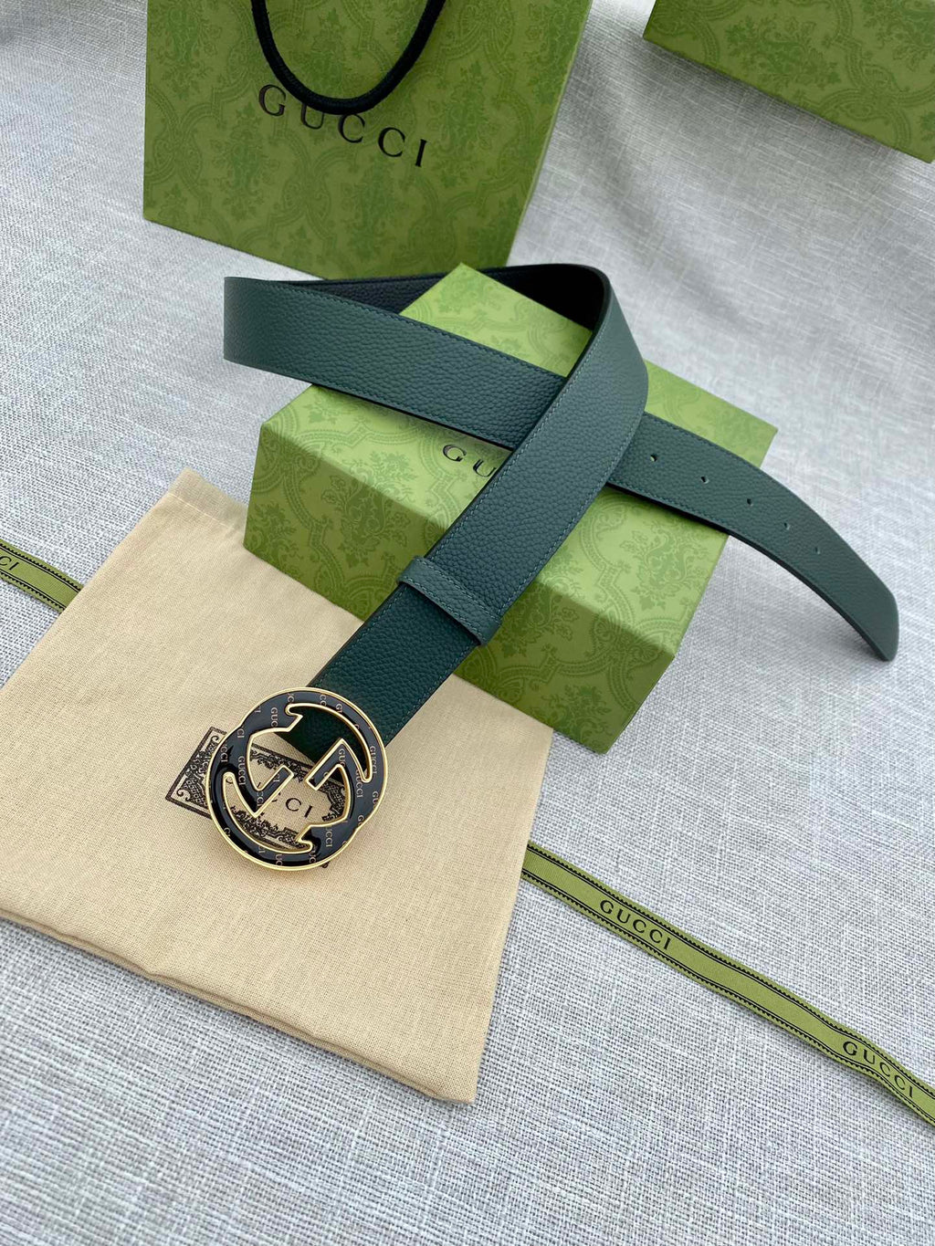Dark green leather belt with round GG logo buckle, laid flat with end strap