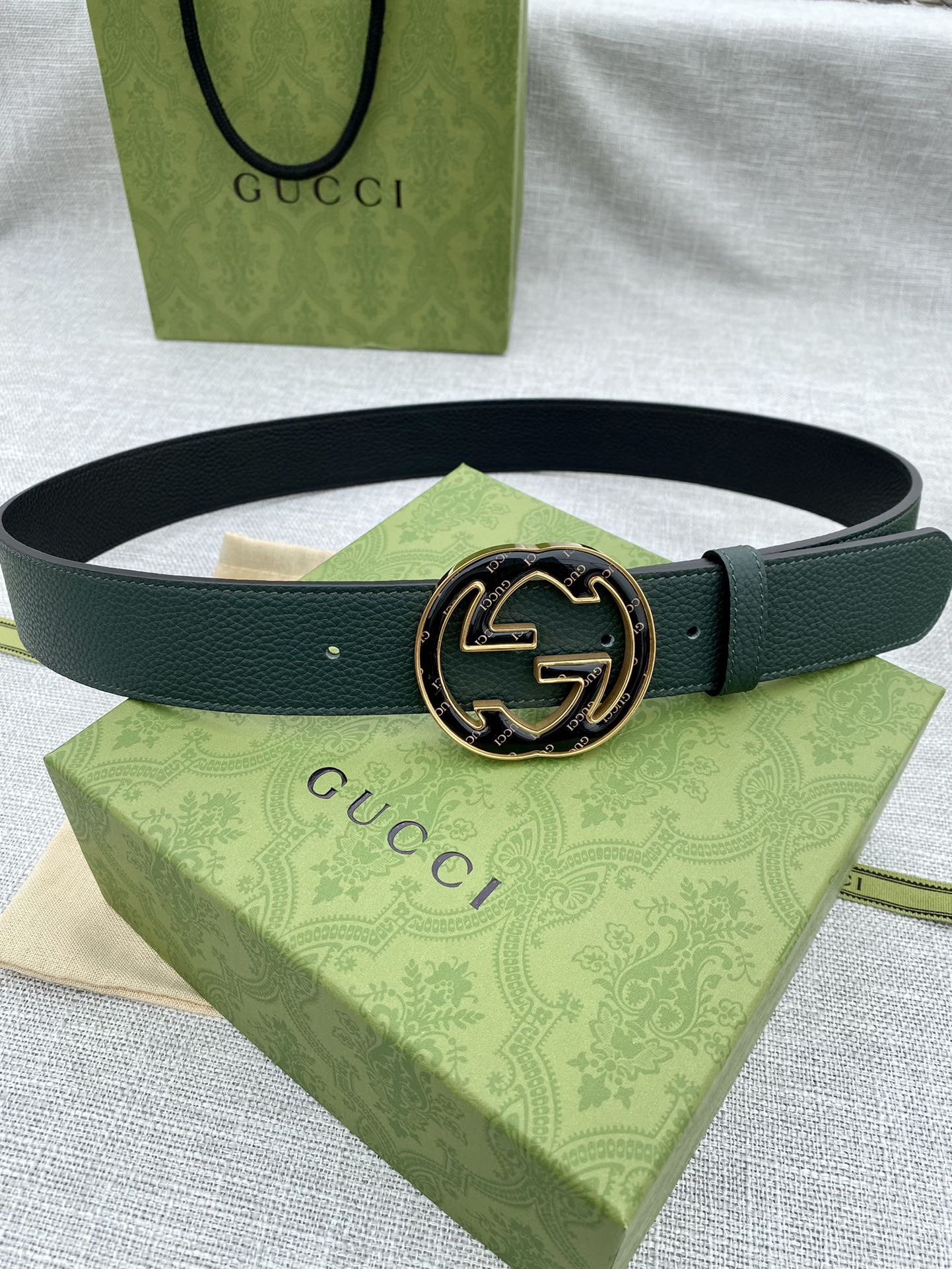 Dark green leather belt with round GG logo buckle, gold-tone edges and dark enamel