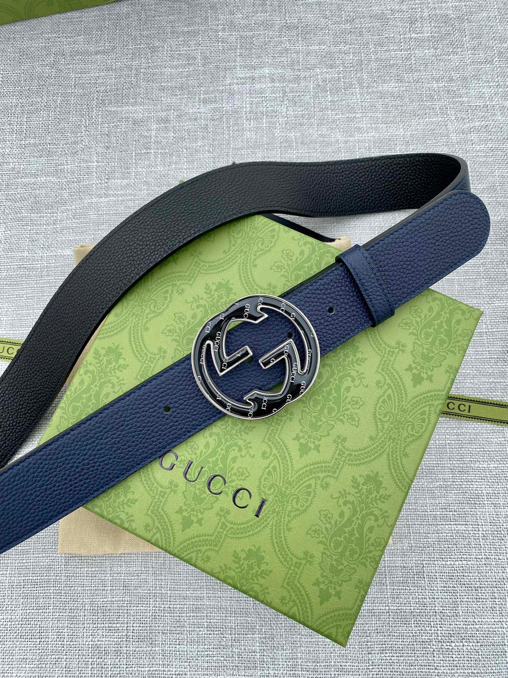 Navy blue leather belt with round double-G logo buckle on green tissue