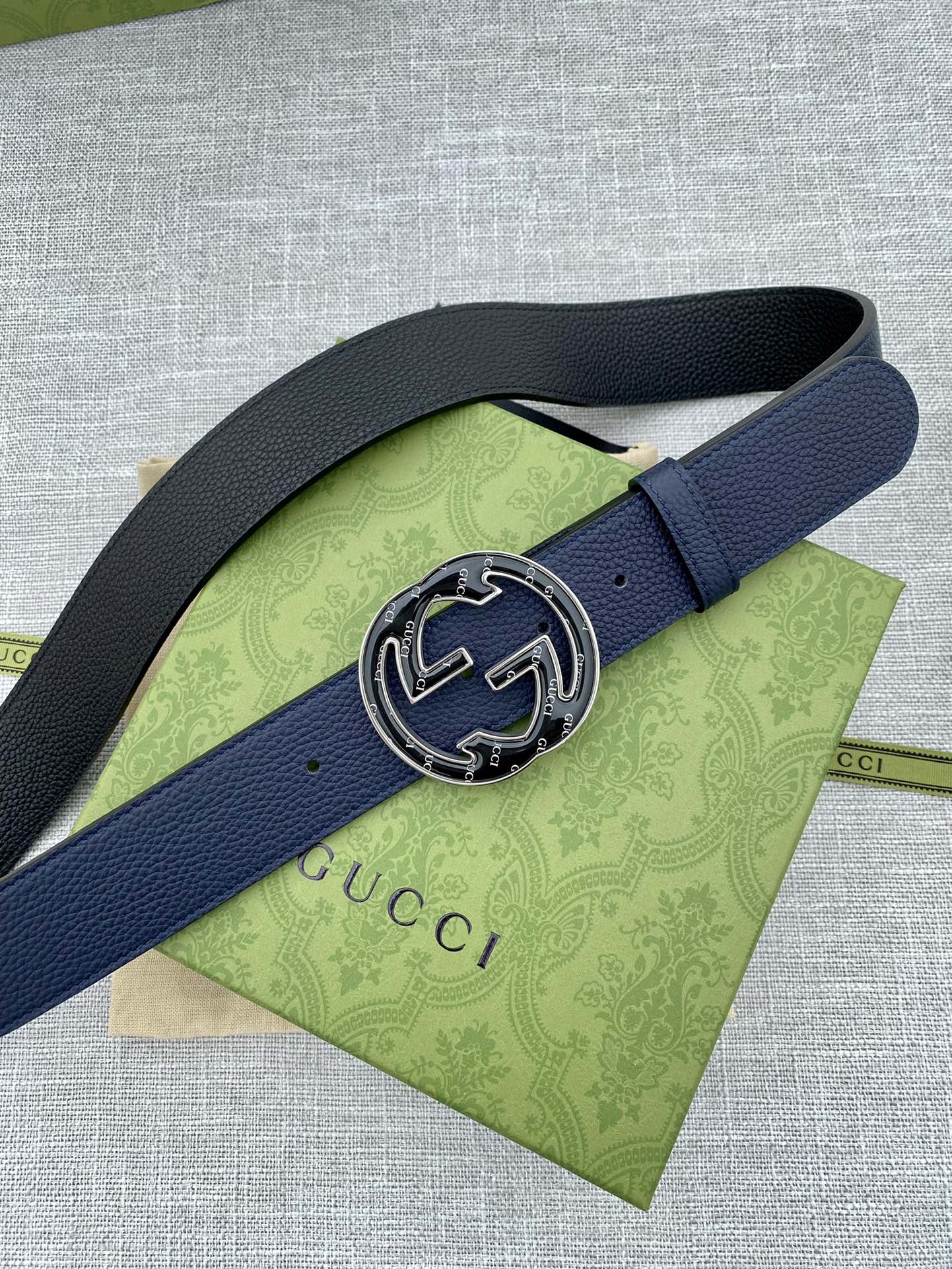 Navy blue leather belt with round double-G logo buckle on green tissue