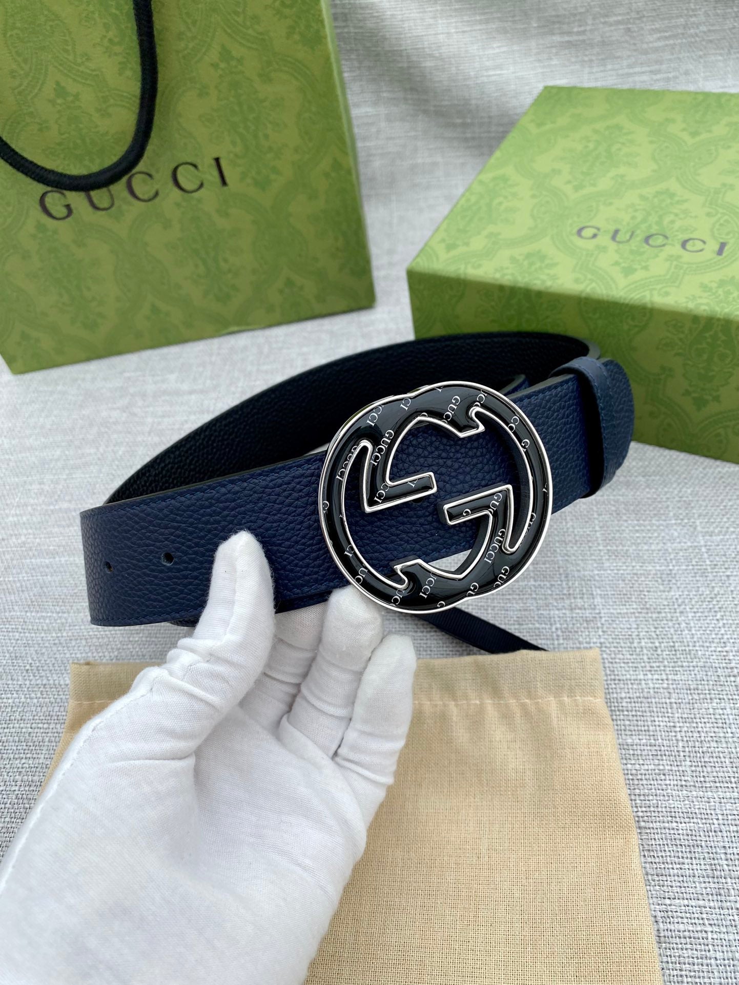 Navy blue leather belt with round double-G logo buckle, gloved hand