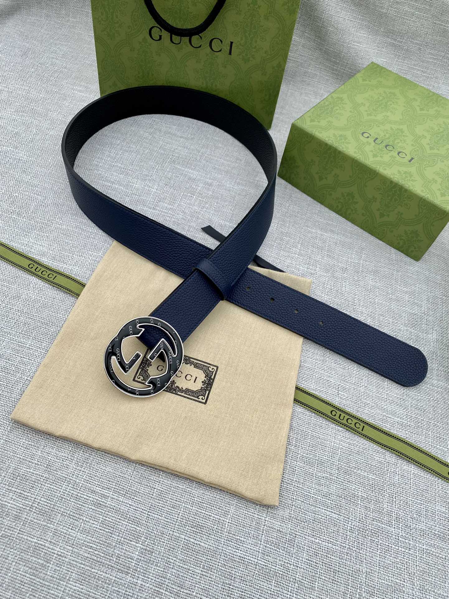 Navy blue leather belt with round double-G logo buckle, angled view