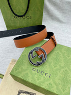 Tan leather belt with round logo buckle, laid across green and beige bags.