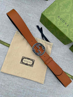 Tan leather belt with round logo buckle, laid flat on a beige cloth pouch.