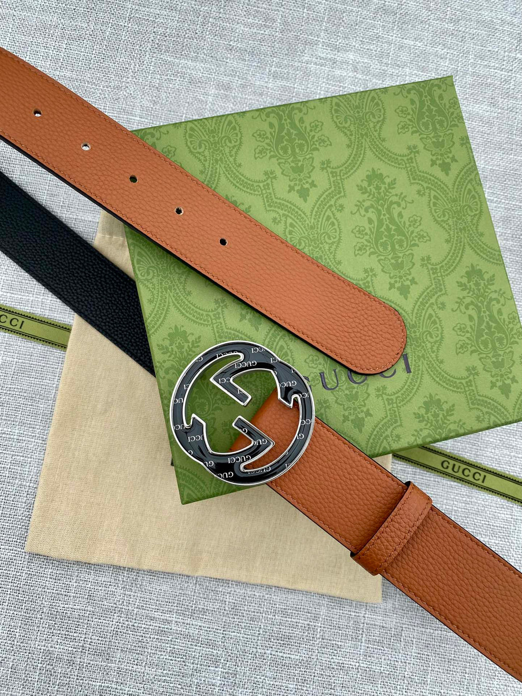 Tan leather belt close-up of round logo buckle and perforated sizing holes.