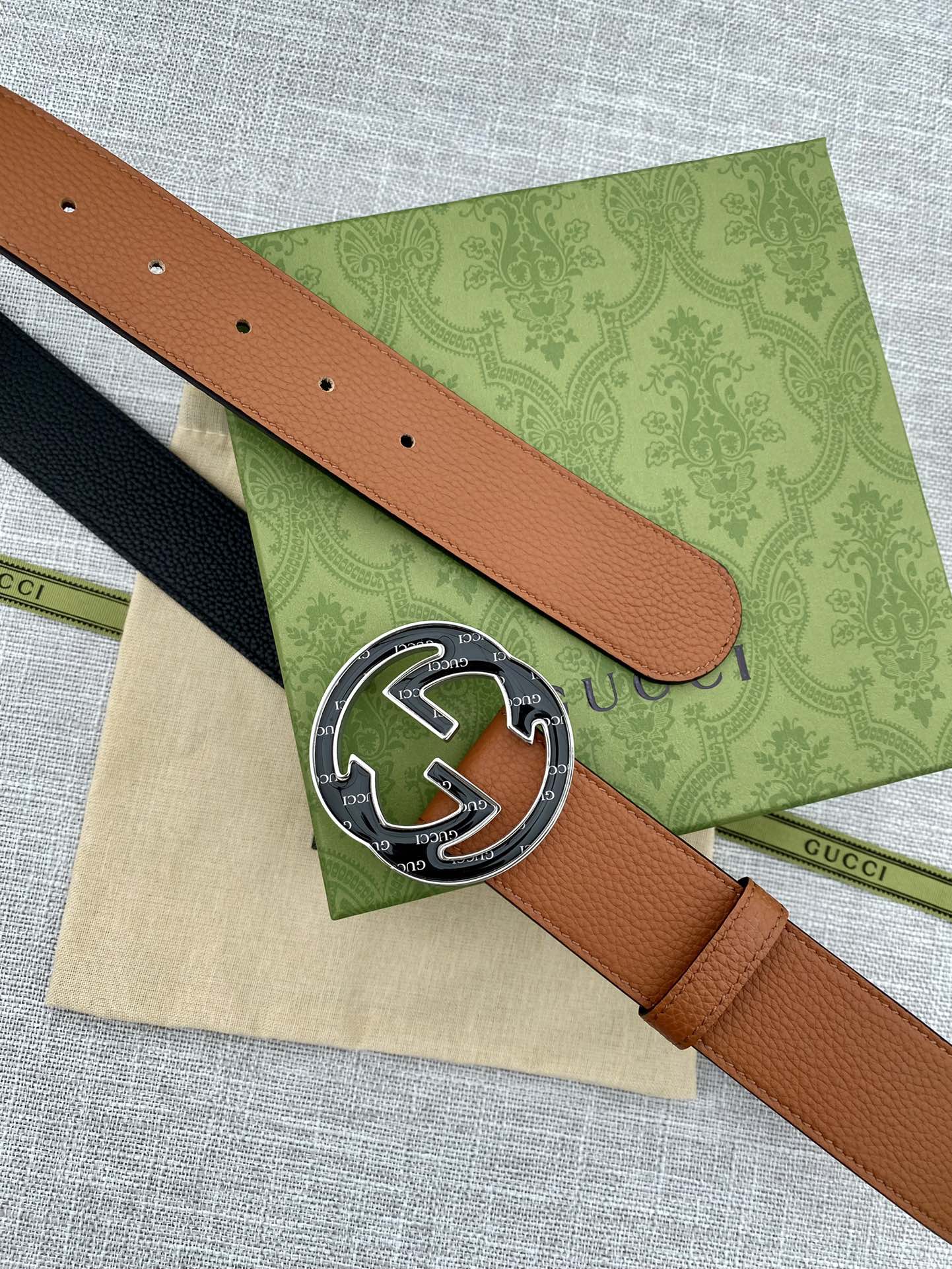 Tan leather belt close-up of round logo buckle and perforated sizing holes.