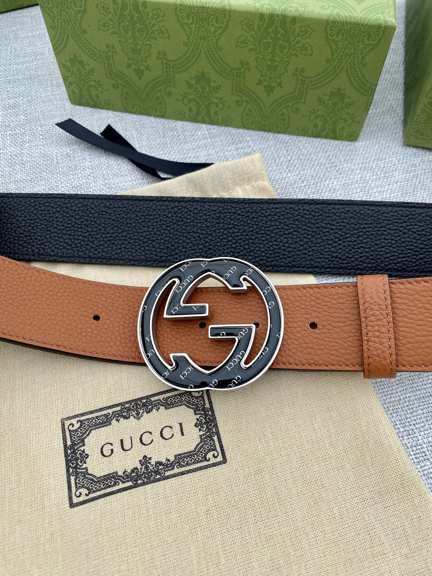 Tan leather belt with round metal logo buckle and dark underside strap visible.