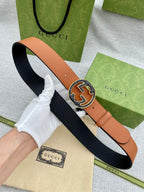 Tan leather belt with round logo buckle, shown with navy underside lining.