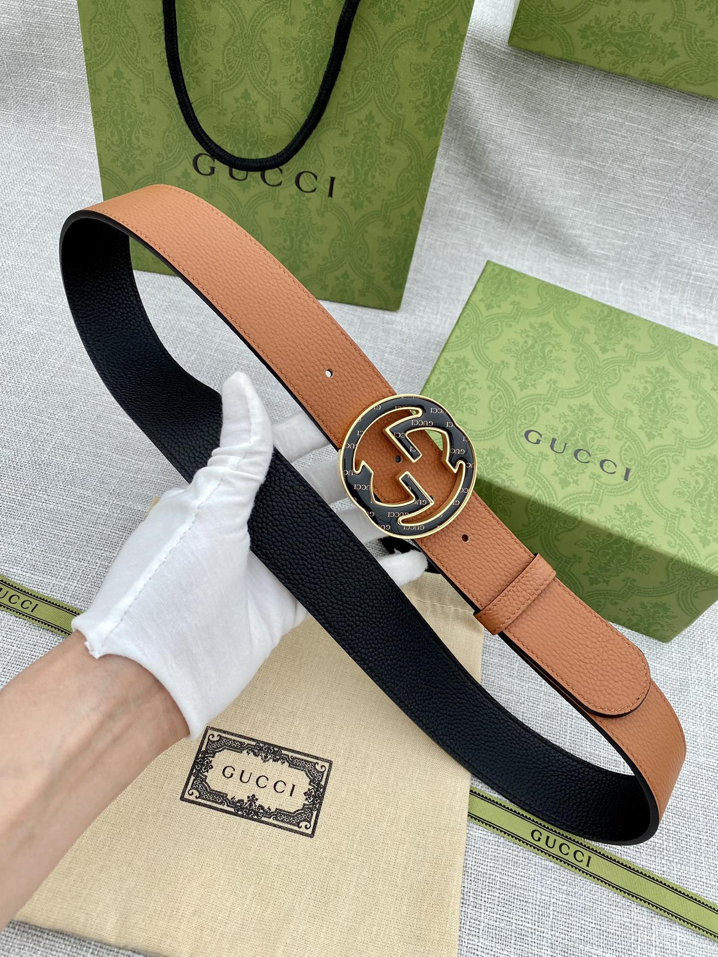 Tan leather belt with round logo buckle, shown with navy underside lining.