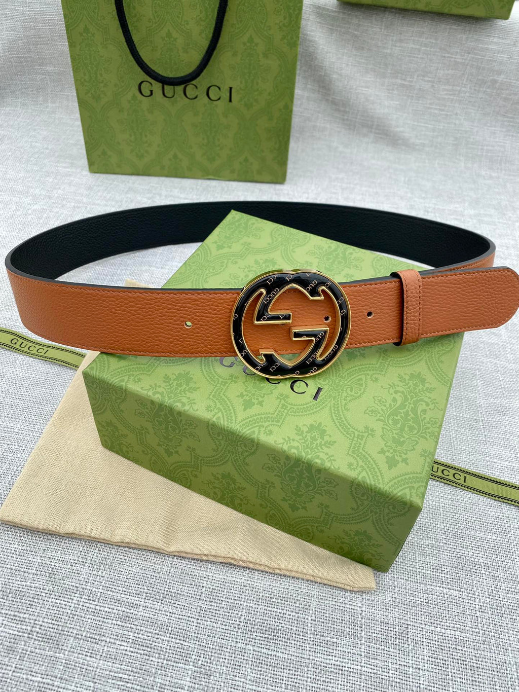 Tan leather belt with round metal logo buckle and small sizing holes.