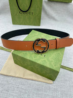 Tan leather belt with round metal logo buckle and small sizing holes.