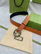 Tan leather belt with round logo buckle and adjustable strap with stitching.