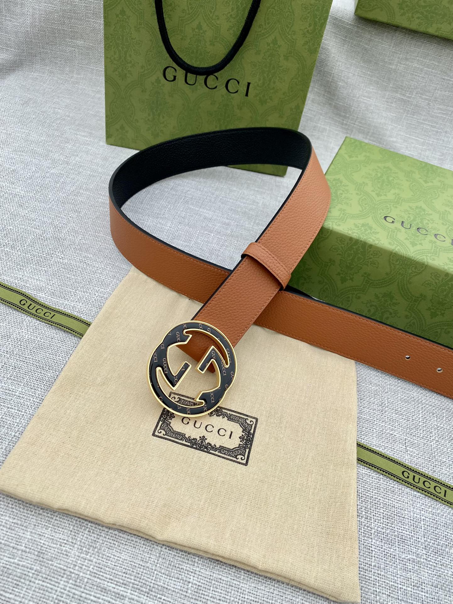 Tan leather belt with round logo buckle and adjustable strap with stitching.