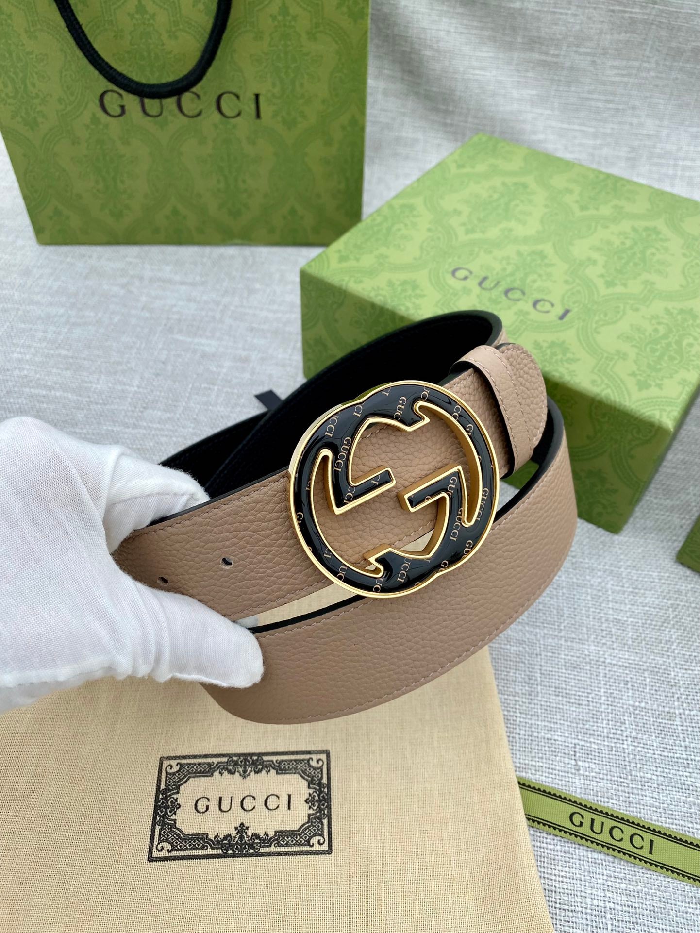 Tan leather belt with round GG logo buckle held with white glove