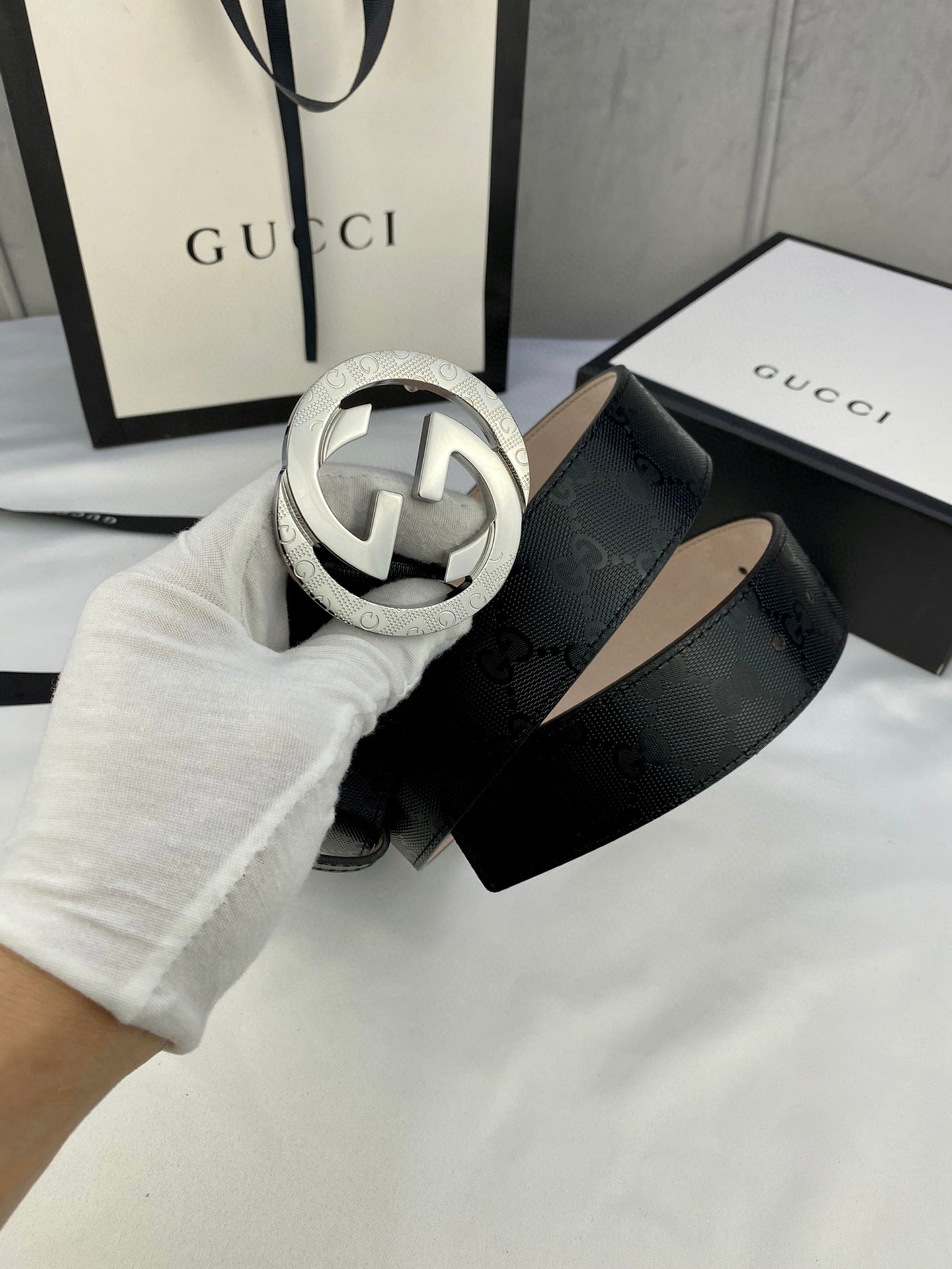 Black monogram leather belt with silver double-G buckle, strap curved