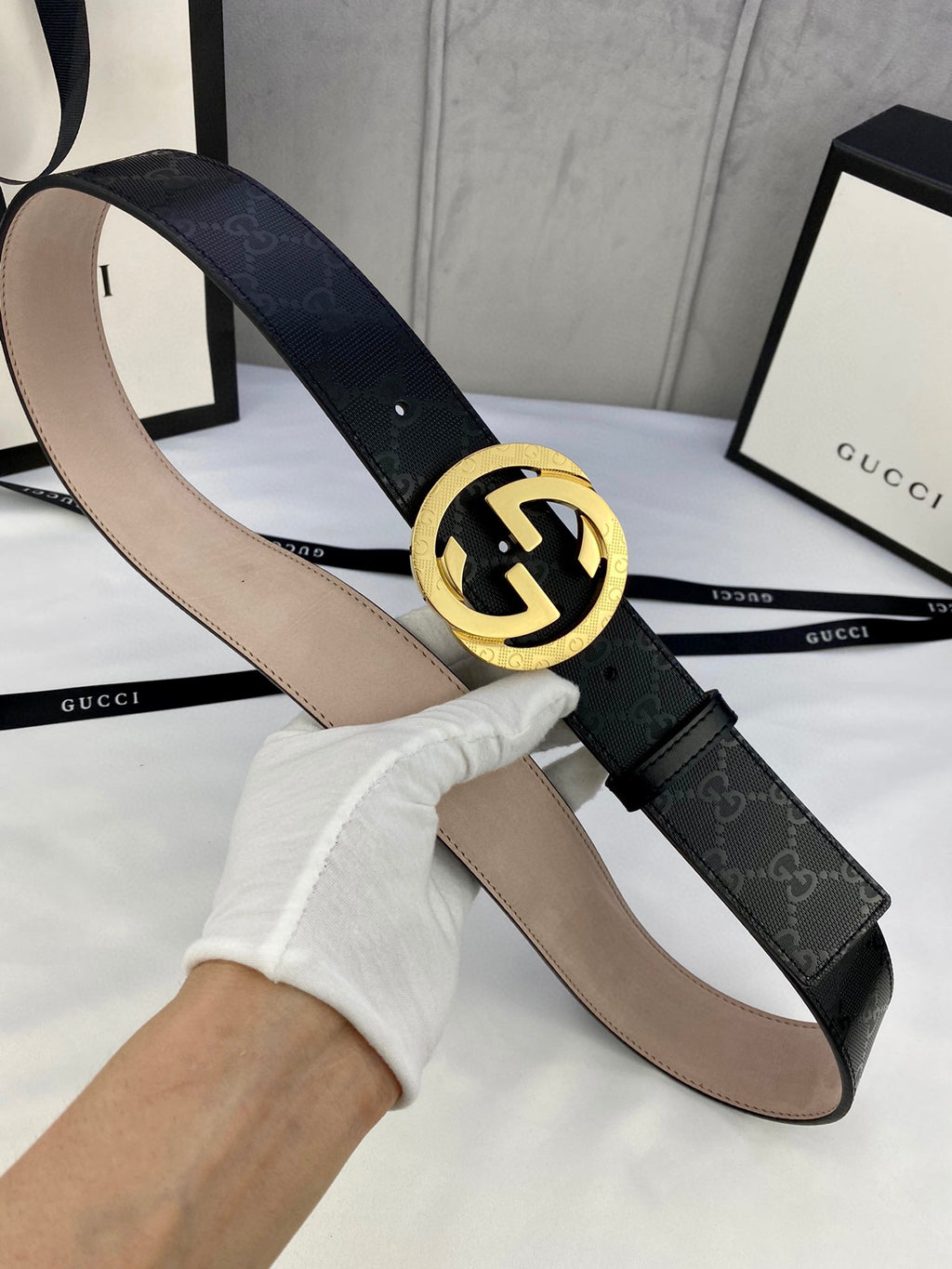 Black monogram leather belt with gold double-G buckle, strap held up