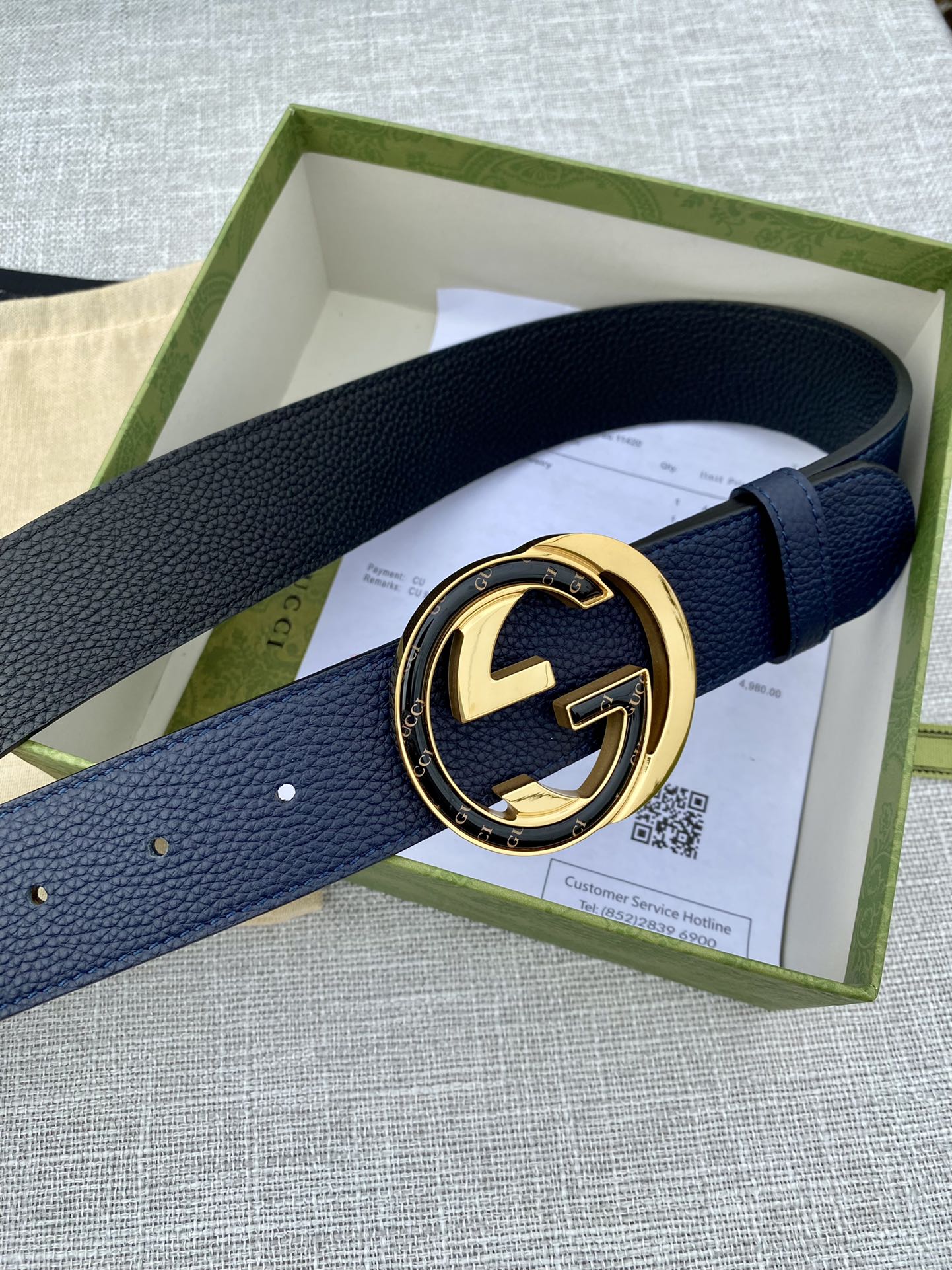 Navy leather belt with gold-tone GG-style buckle on retail box insert