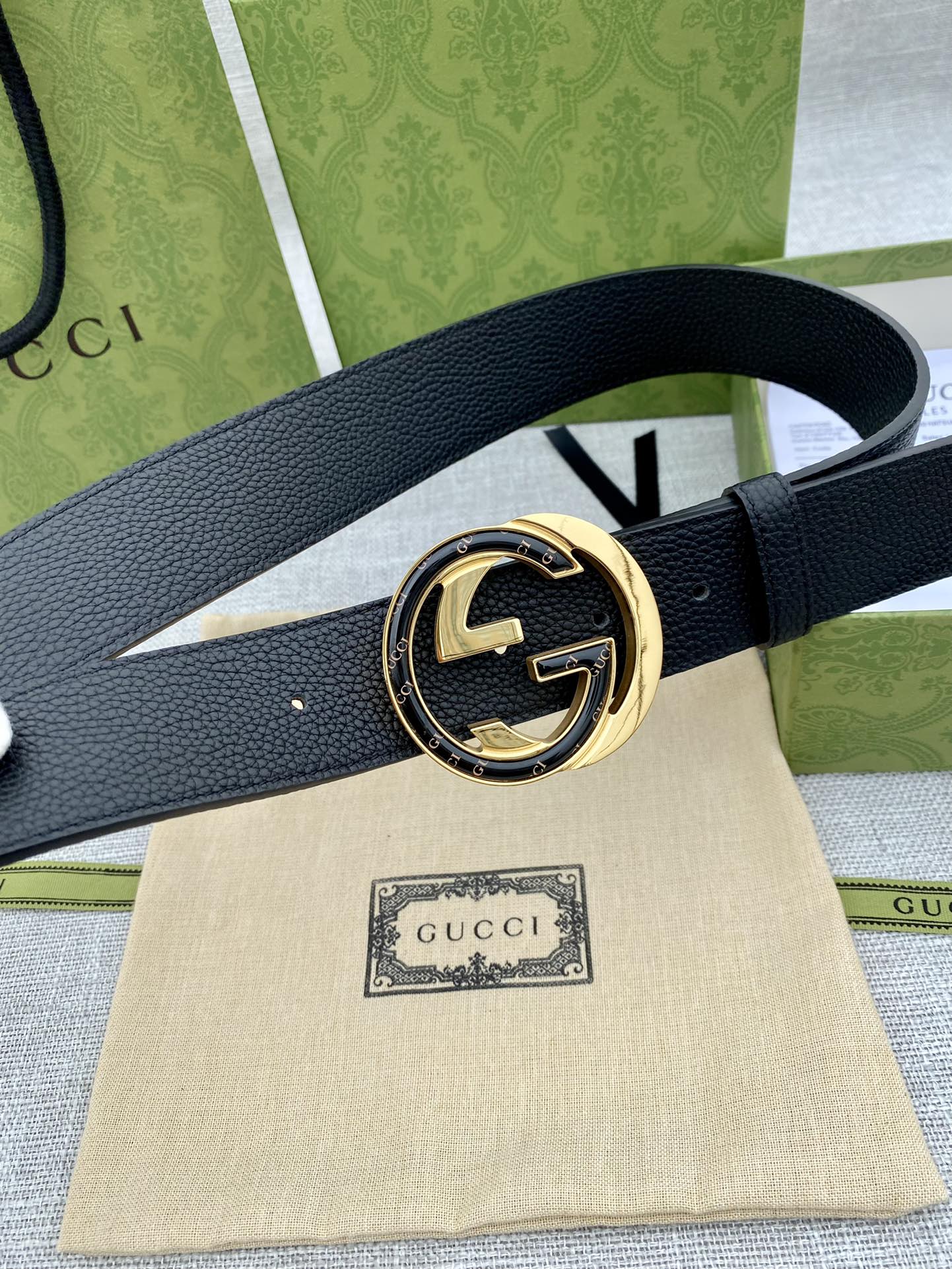 Black leather belt with gold-tone round buckle set on a light fabric pouch