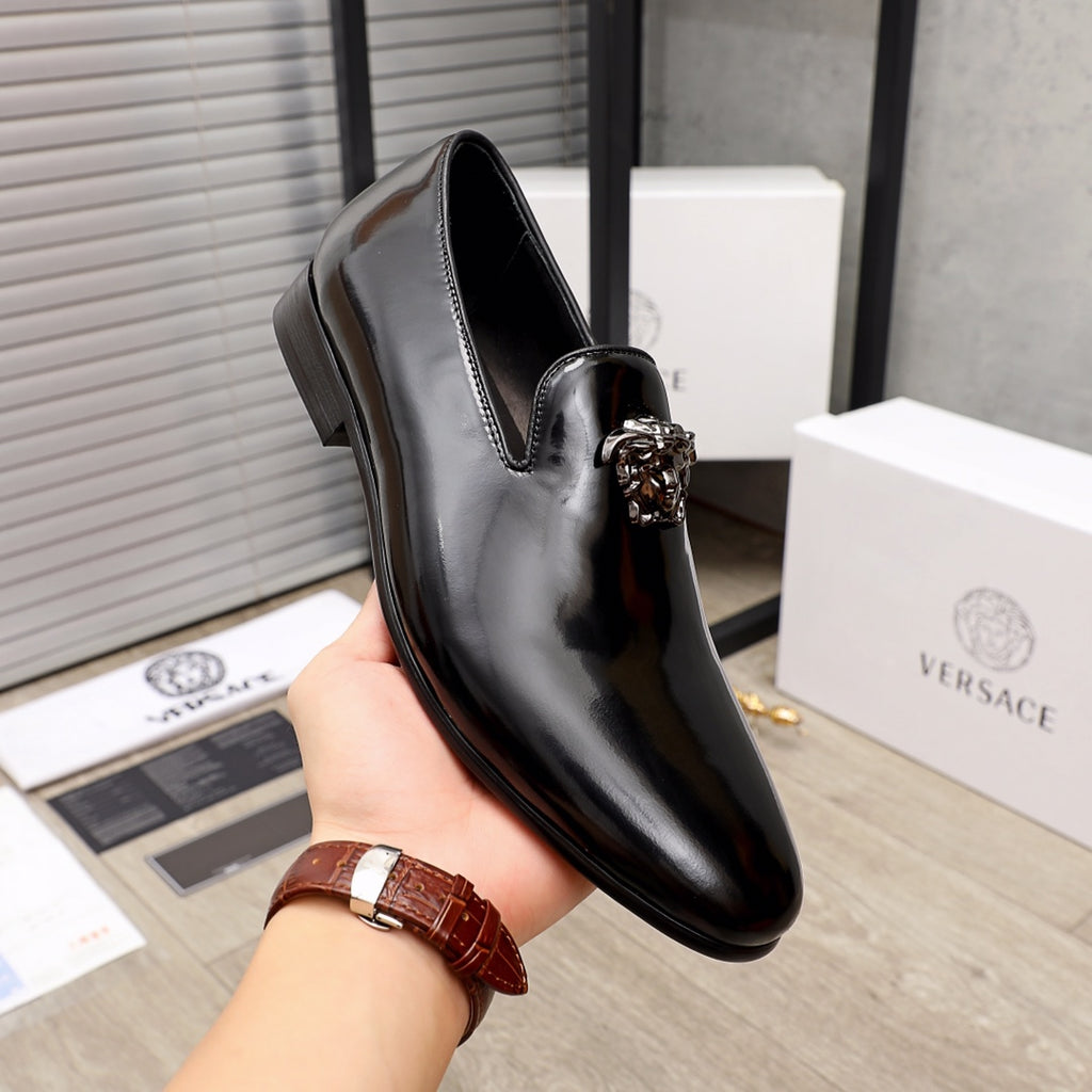 Versace black glossy loafers held in hand, with lion-head metal detail