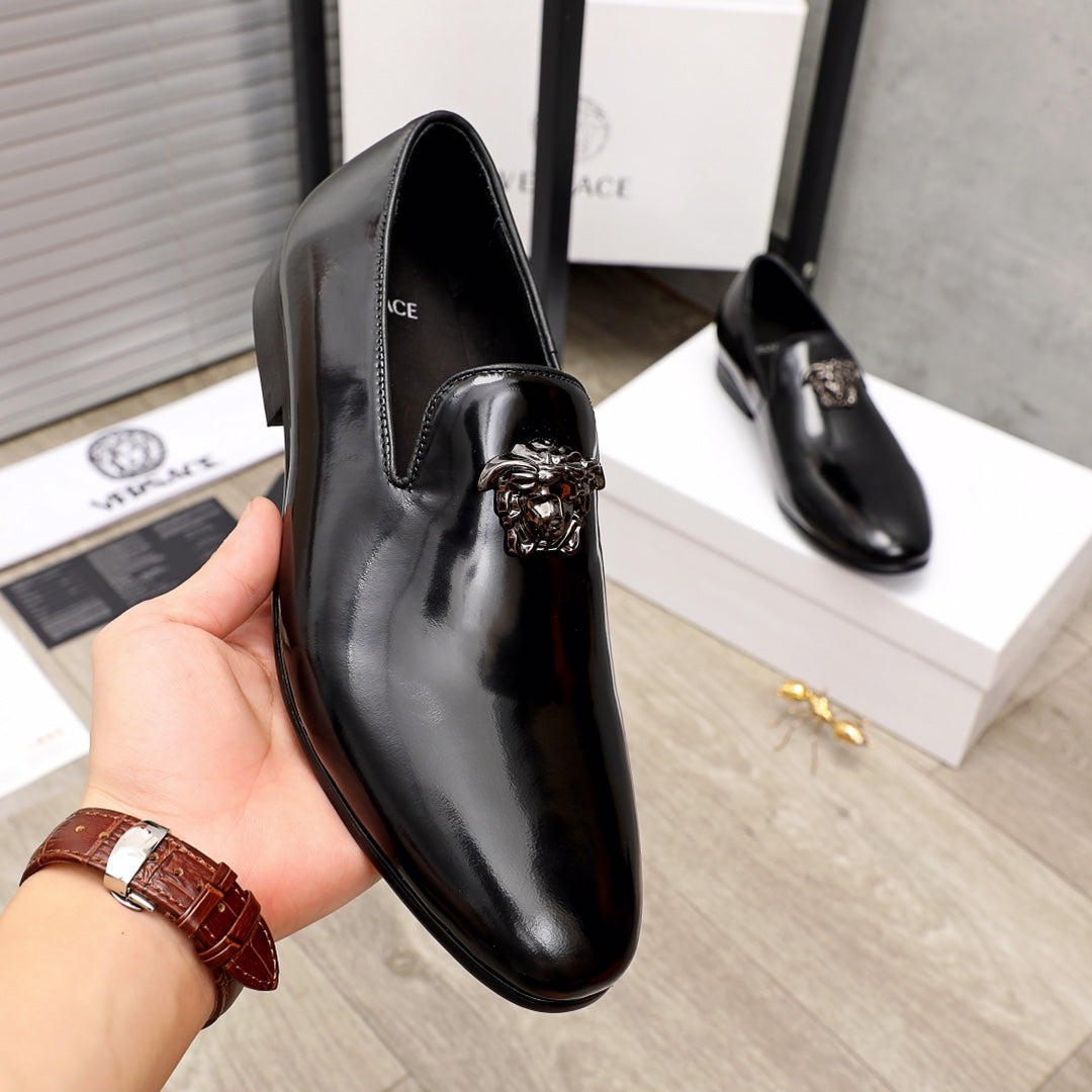Versace black patent leather loafer with lion-head ornament, shown close on hand