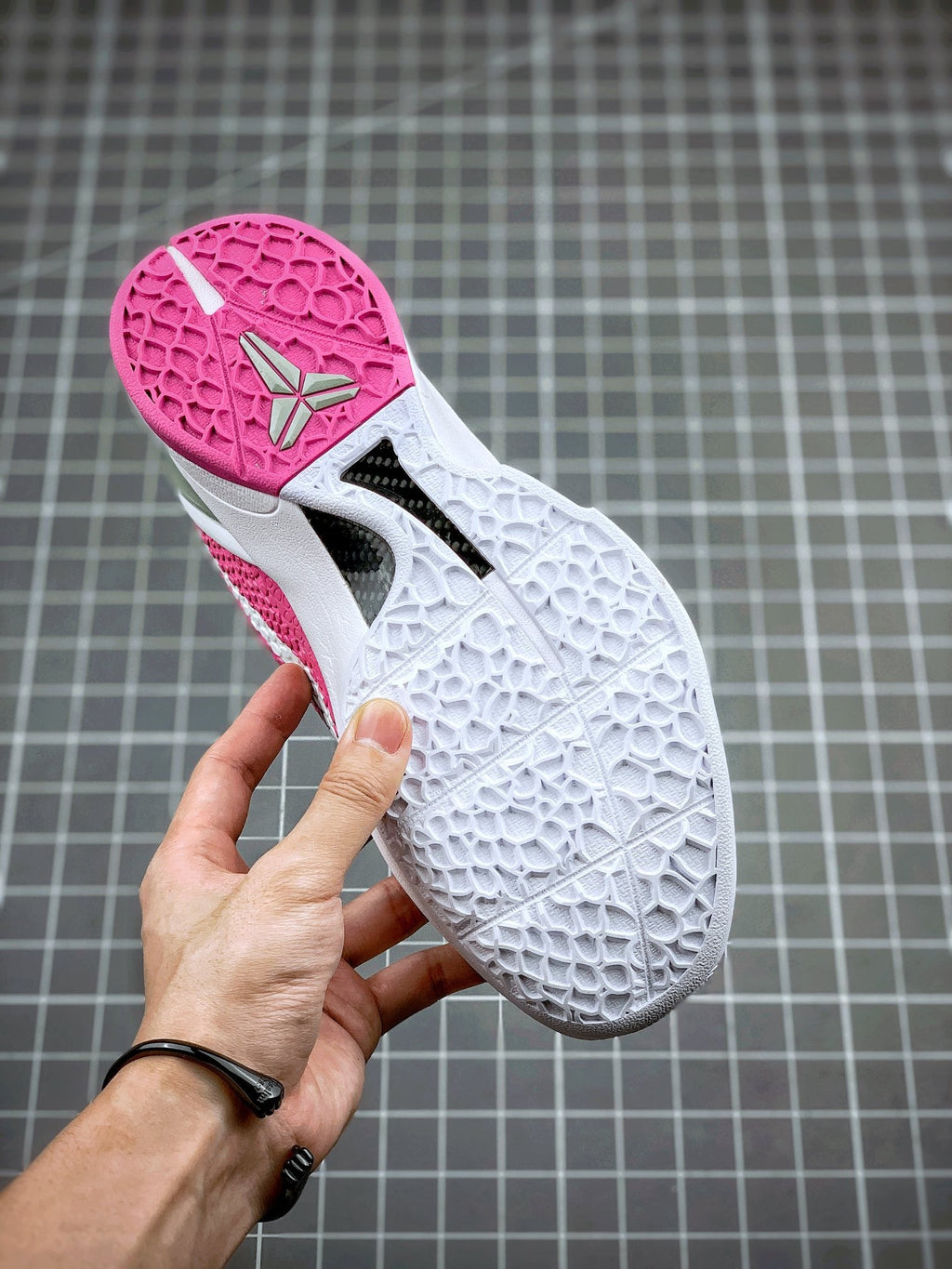 Pink-and-white basketball sneaker showing textured outsole tread, bottom view