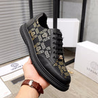 Versace sneakers held in hand, black leather with gold pattern stripe and lace-up